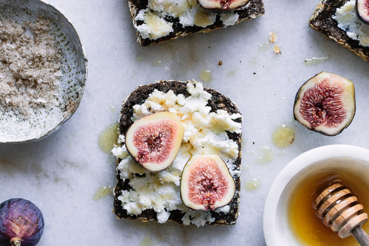 A piece of breakfast bread with cheese, figs, and honey on a table.