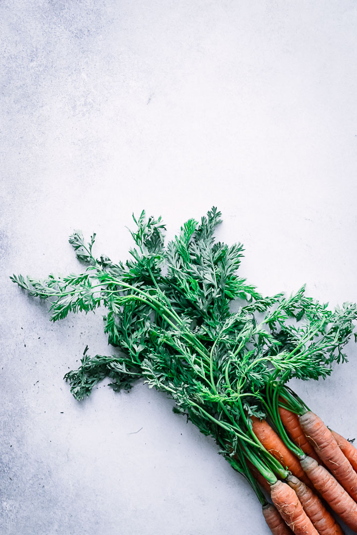 A bunch of carrots with bright green stems on a white table.