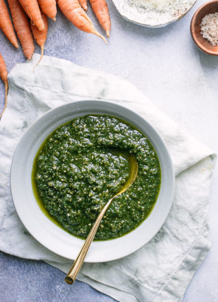 A bowl of pesto made with carrot greens on a white napkin on a blue table.