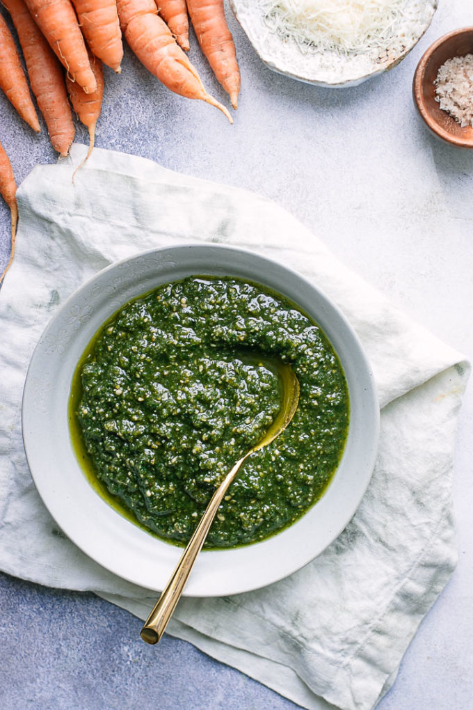 A bowl of pesto made with carrot greens on a white napkin on a blue table.