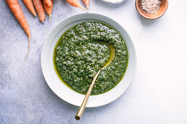 A white bowl of pesto on a white table table.