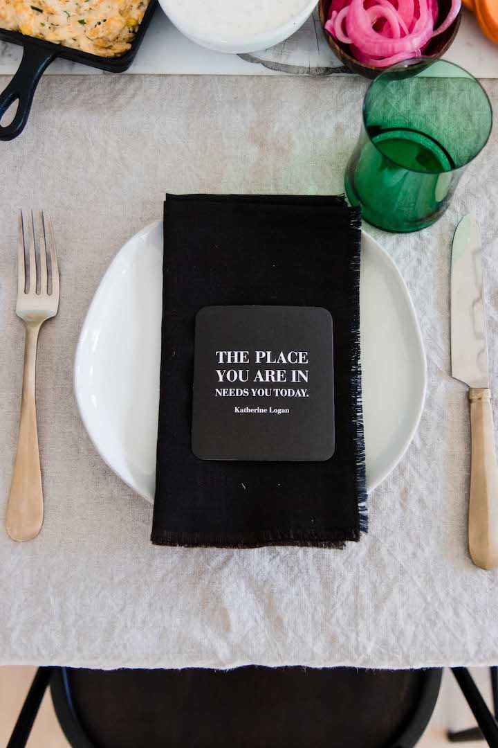 A photo of a white plate with a black napkin with a green glass.