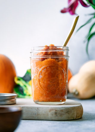 A jar of homemade pumpkin puree on a blue table with a gold spoon