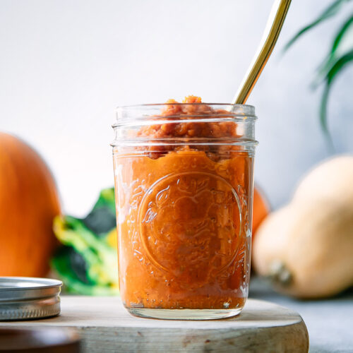 A jar of homemade pumpkin puree on a blue table with a gold spoon