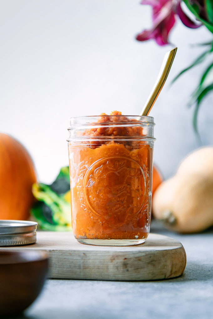 A jar of homemade pumpkin puree on a blue table with a gold spoon