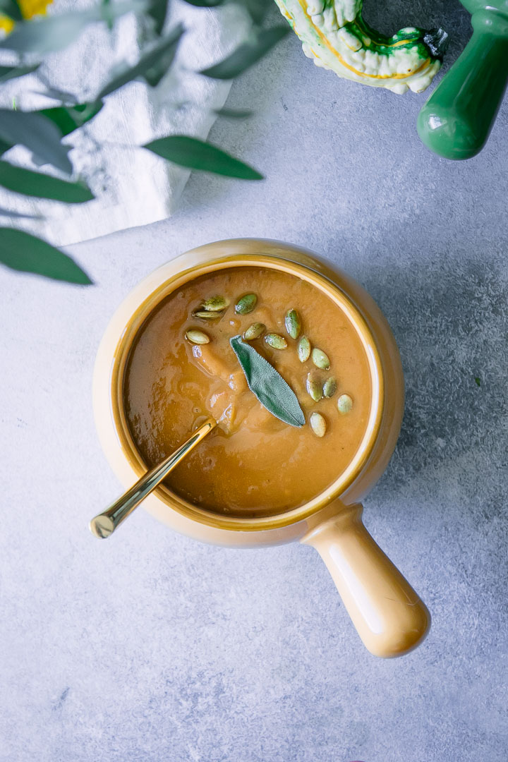 Orange pumpkin soup in a yellow bowl with a gold spoon