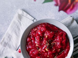 Red cranberry sauce on a blue table with flowers and the words "maple bourbon cranberry sauce" in black writing