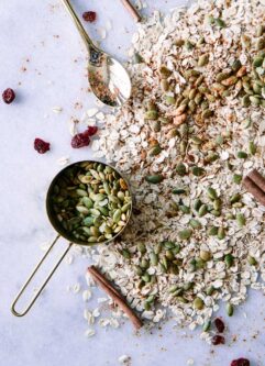 oats, pumpkin seeds, cranberries, and cinnamon on white marble background