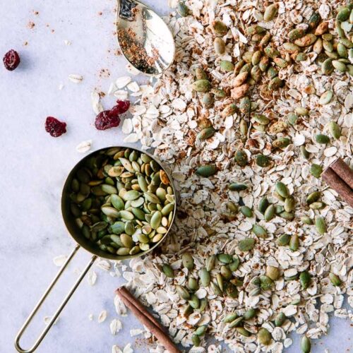 oats, pumpkin seeds, cranberries, and cinnamon on white marble background