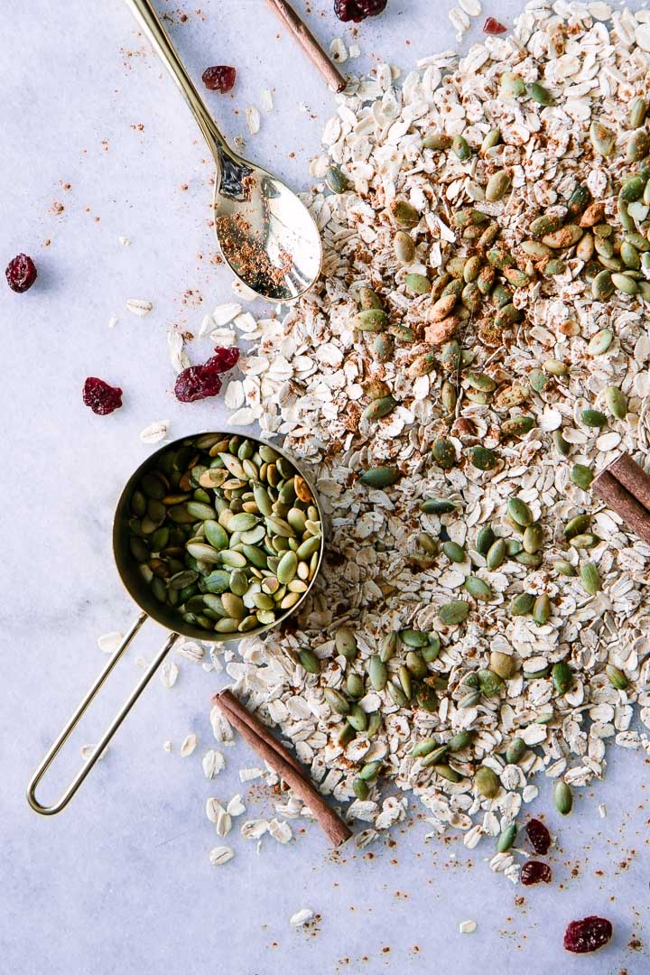 oats, pumpkin seeds, cranberries, and cinnamon on white marble background
