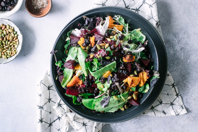 a fall vegetable salad in a black bowl on a white table