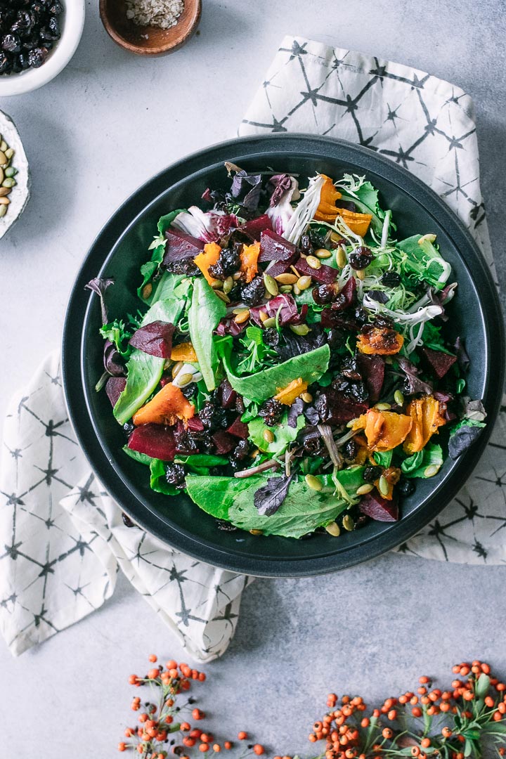 green salad with orange squash, red beets, cranberries, and a white napkin