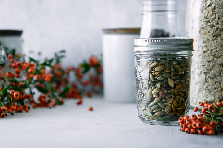 A jar of pumpkin seeds on a table with orange flowers