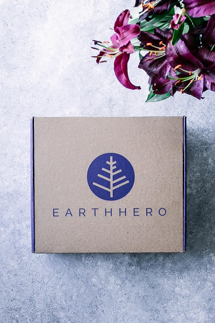 A cardboard Earth Hero subscription box on a blue table with flowers
