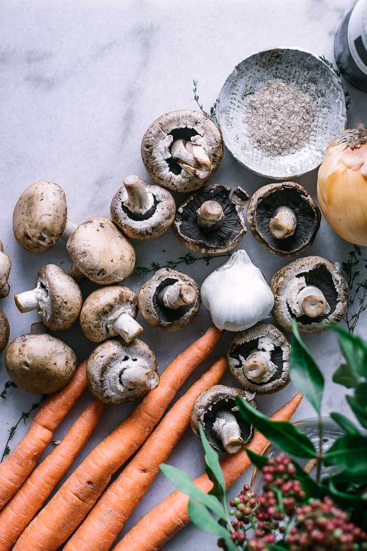 carrots, mushrooms, garlic, onion, and salt on a marble countertop