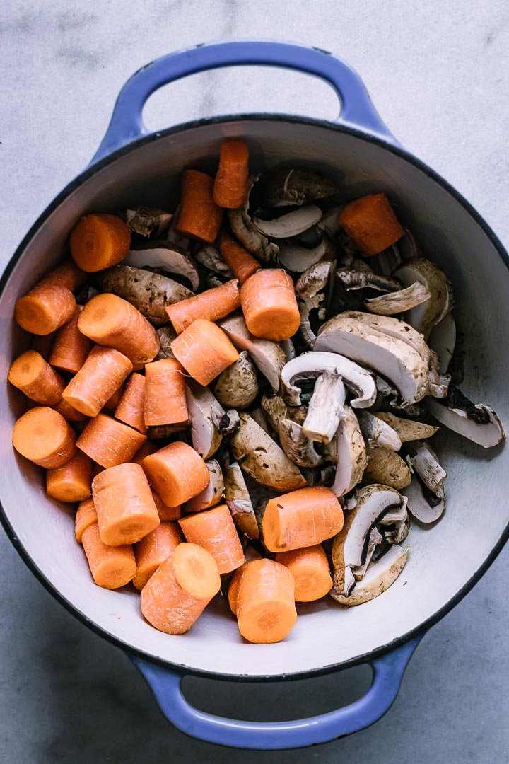 a blue dutch oven with cut mushrooms and carrots