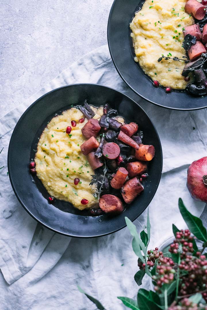 a black bowl with polenta and braised mushrooms and carrots