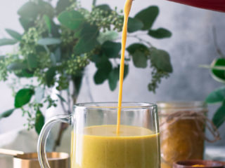 golden milk pouring into a glass coffee mug with words "cinnamon golden milk latte" in black writing