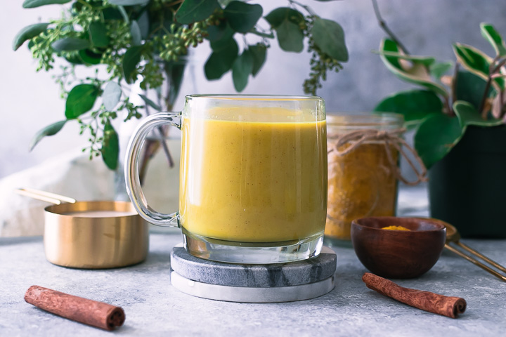 a yellow golden milk latte in a glass mug with cinnamon sticks