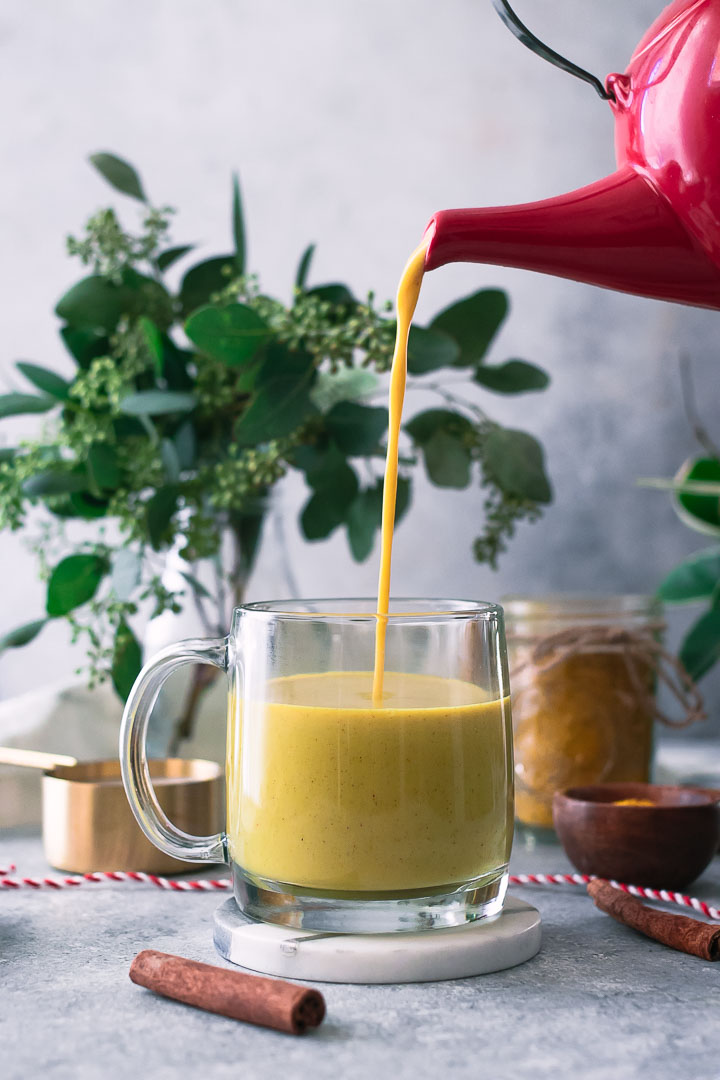 yellow turmeric golden milk latte on a white table with cinnamon and milk