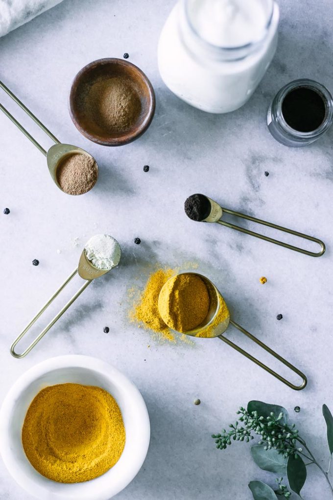 turmeric, cardamom, nutmeg, coconut powder, cinnnamon, and other golden milk spices on a marble countertop