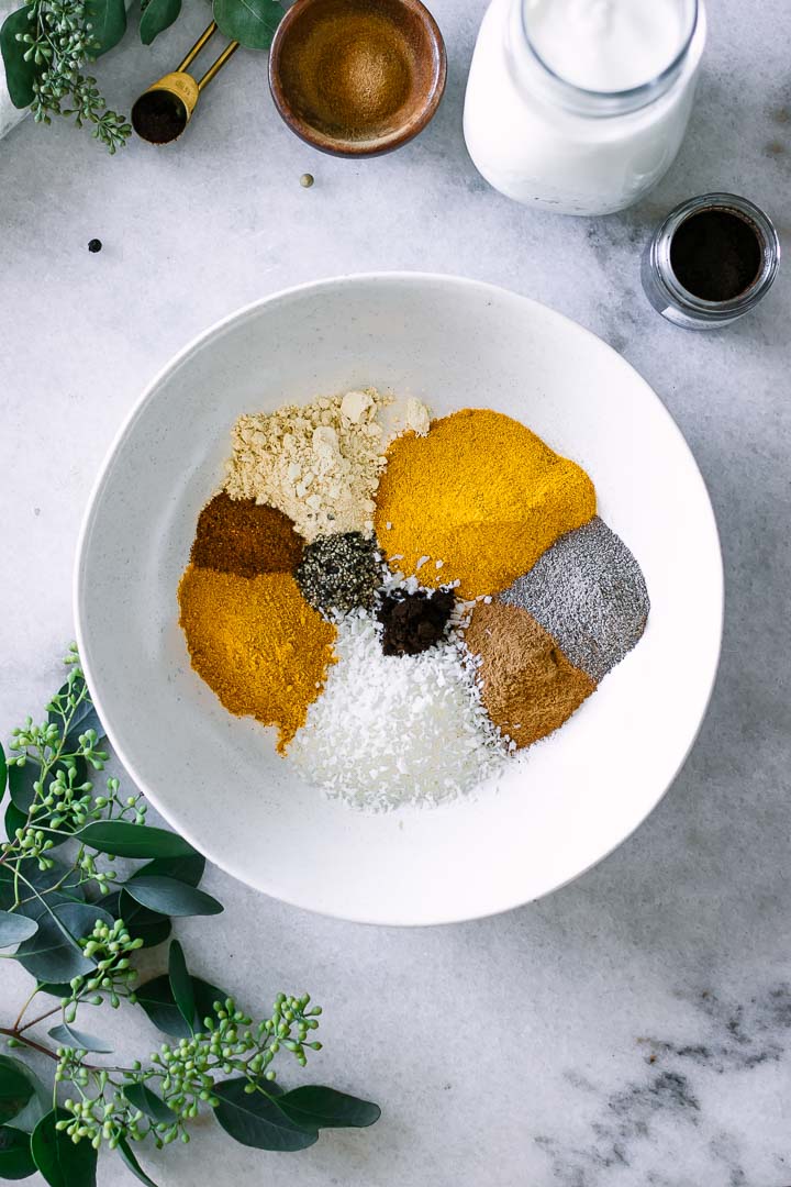 Turmeric, ginger, coconut, cinnamon, black pepper, nutmeg, and cardamom in a white bowl.