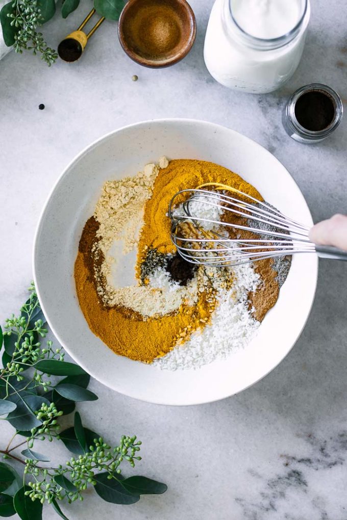a hand mixing golden milk spices in a bowl with a whisk