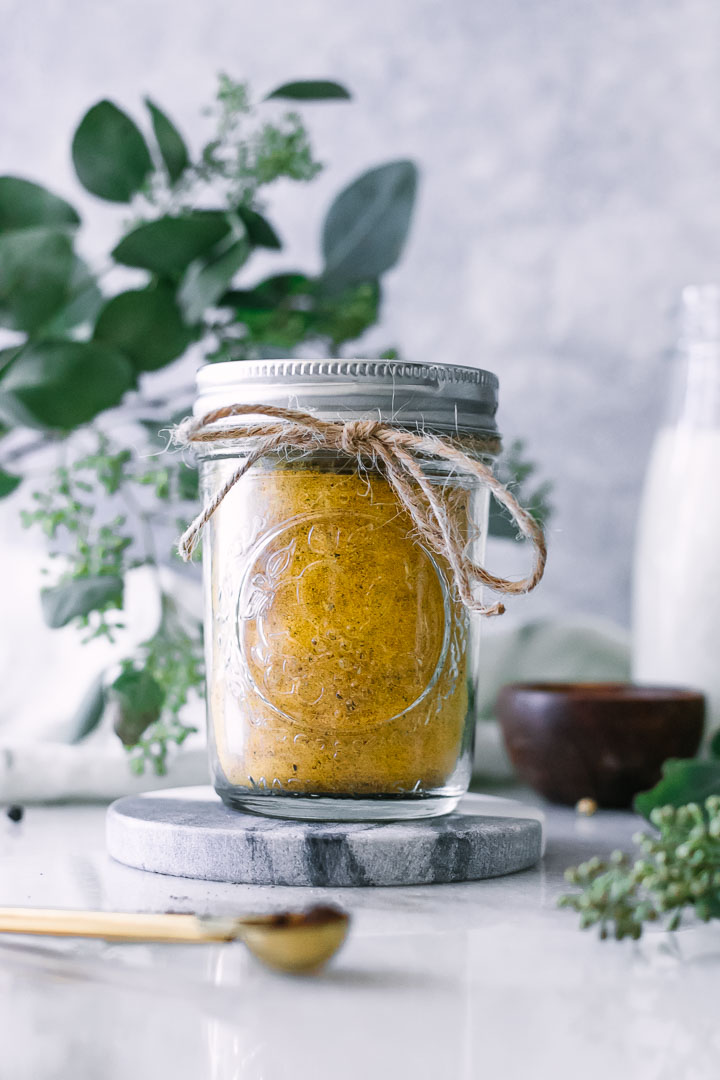 a jar of yellow turmeric golden milk spice mix on a white table with green plants