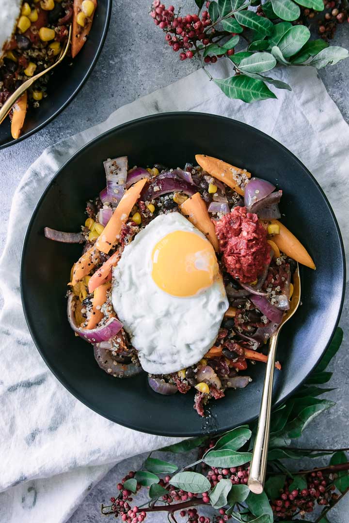 black beans, quinoa, bell peppers, onion, corn, and spicy harissa with an egg on top in a black bowl
