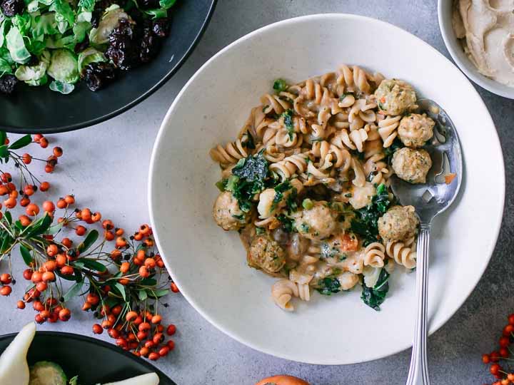 a bowl of pasta with meatballs on a white table with a salad and an orange