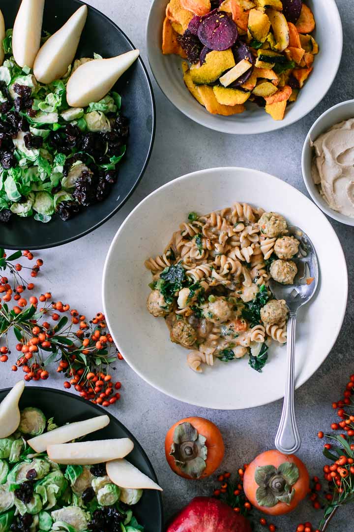 a bowl of pasta with meatballs on a white table with a salad and an orange