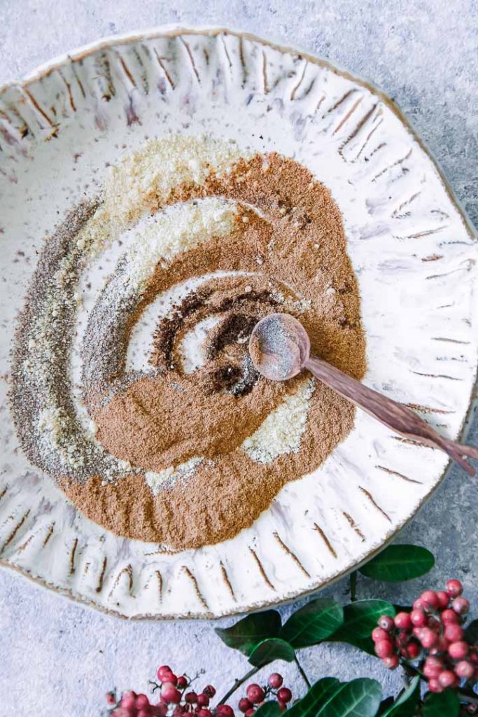 a mixture of chai spices on a white plate with a wooden spoon