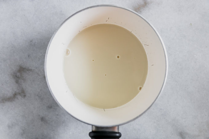 warm oat milk in a small saucepan on a white marble countertop