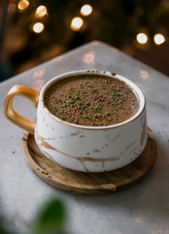 a mocha matcha latte in a white mug on a table with holiday lights in the background