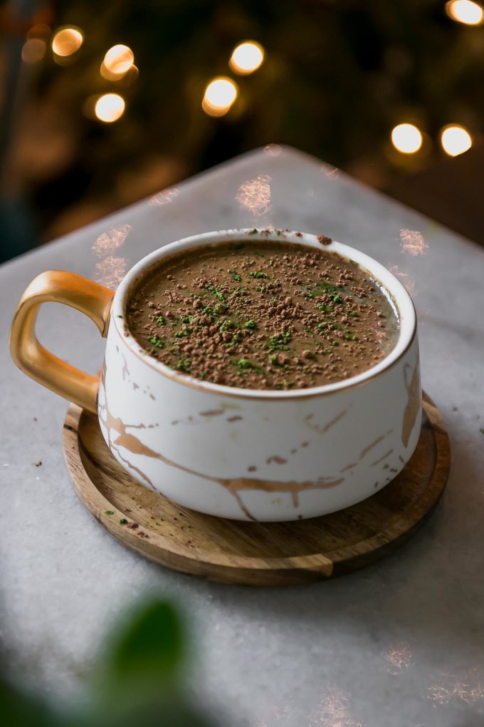 a mocha matcha latte in a white mug on a table with holiday lights in the background