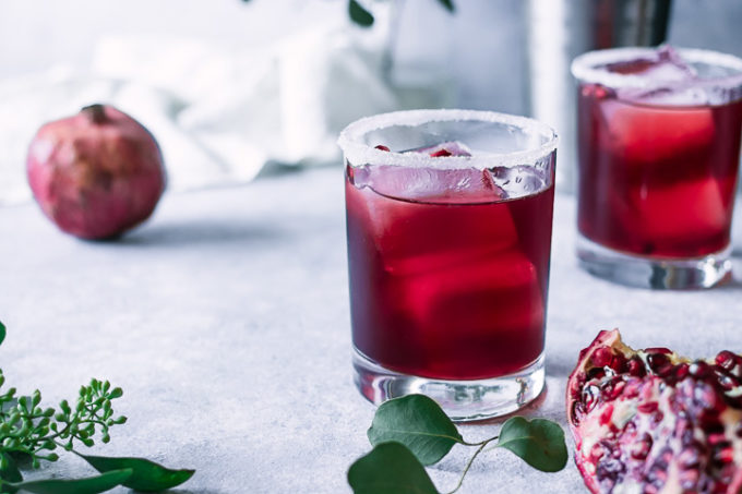 a red cocktail on a white and blue table with a pomegranate