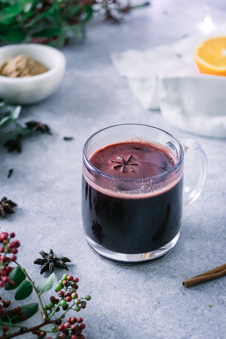 a glass of gluwhein on a blue table with star anise, cinnamon, and cloves