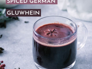 a glass mug with german gluwhein, a spiced mulled red wine, on a blue table with spices and holiday plants