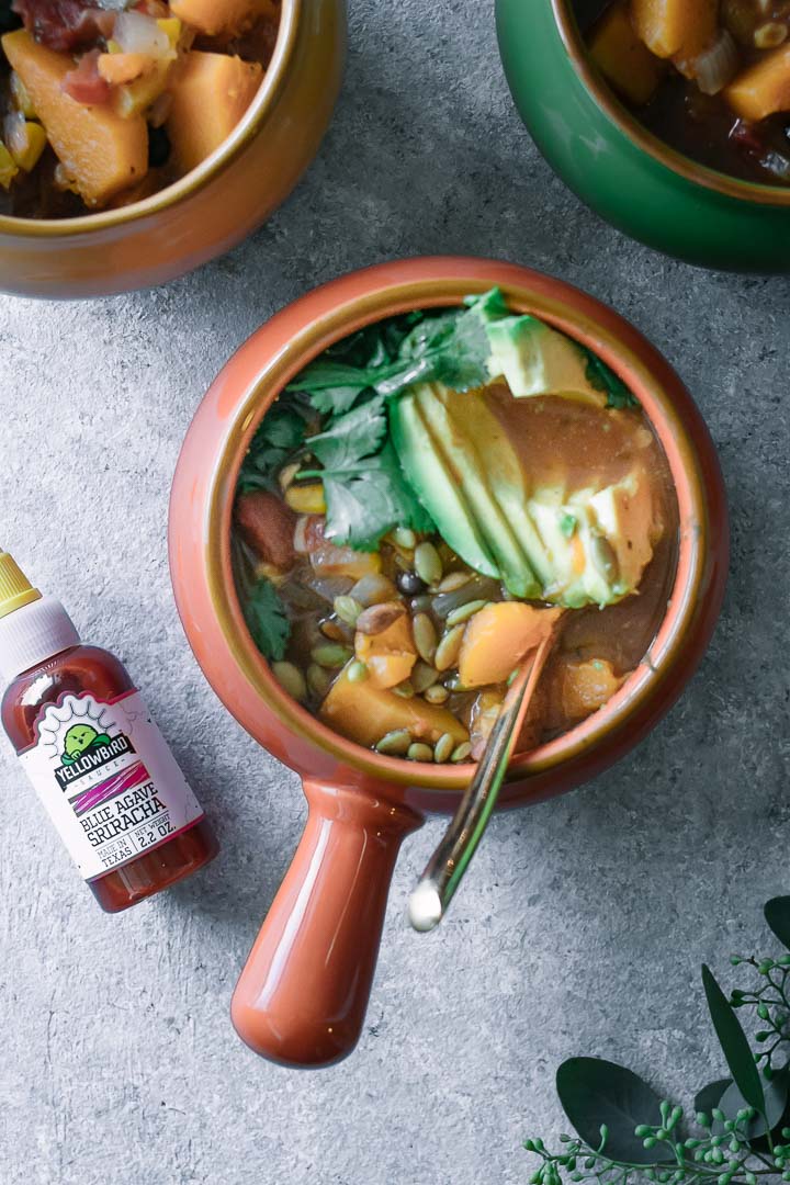 a bowl of vegetable chili with a bottle of Yellowbird hot sauce