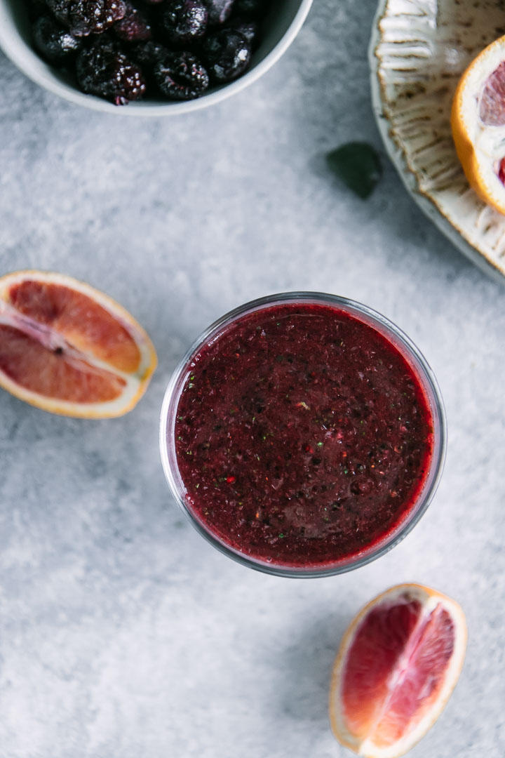 a red and purple smoothie from above with a slice of orange and a plate of frozen berries