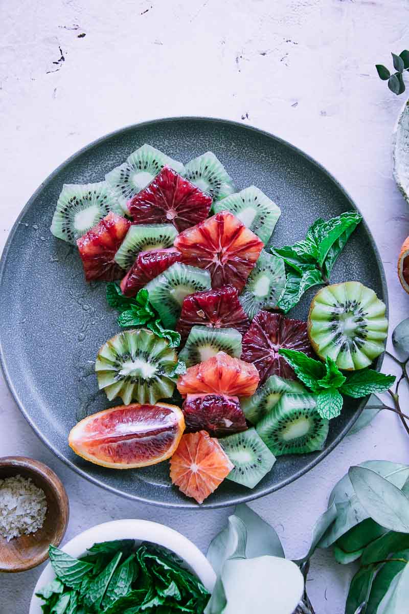 a blue plate with cut oranges, kiwi, and mint leaves