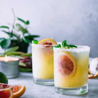 two salted margaritas on a white table with plants and candles