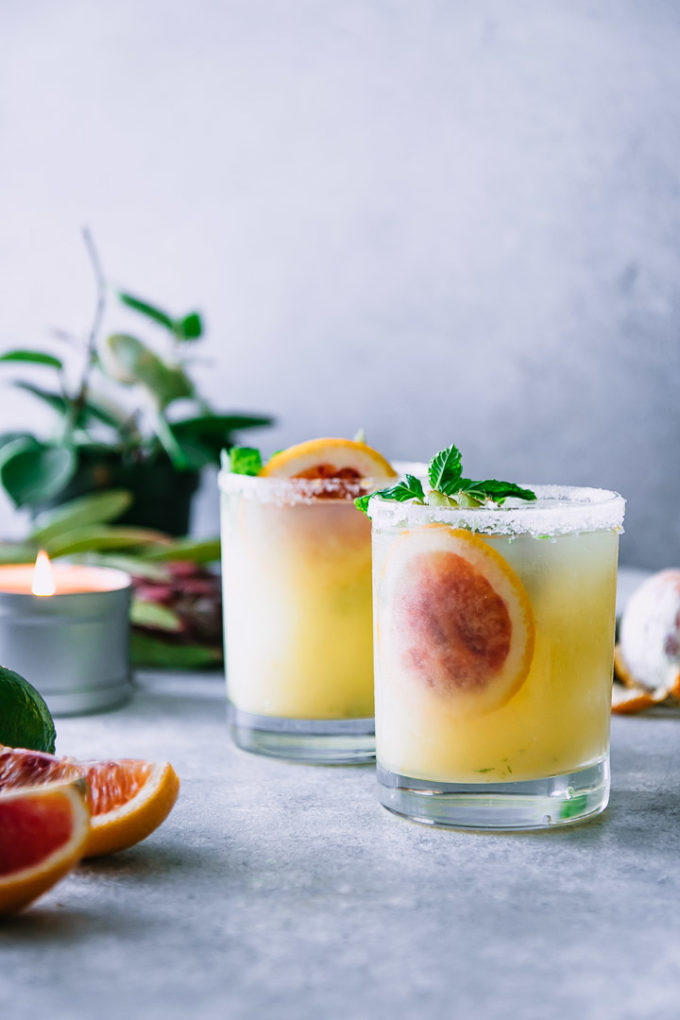 two salted margaritas on a white table with plants and candles