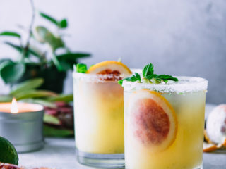 two margaritas on a blue table with the words "blood orange kiwi margaritas" in black writing