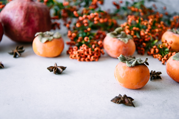 pomegranates and persimmons on a white table with star anise