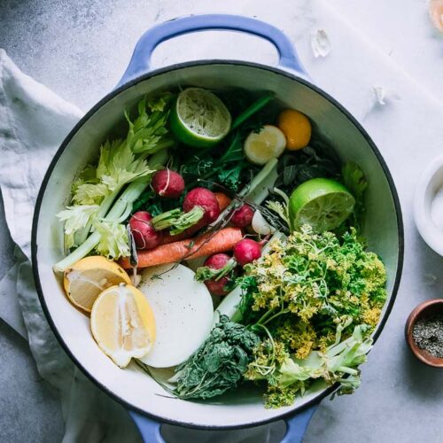 a blue soup pot with bright green red, and yellow vegetables inside on a white table