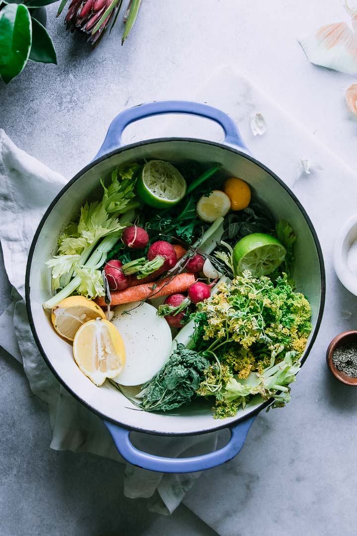 a blue soup pot with bright green red, and yellow vegetables inside on a white table