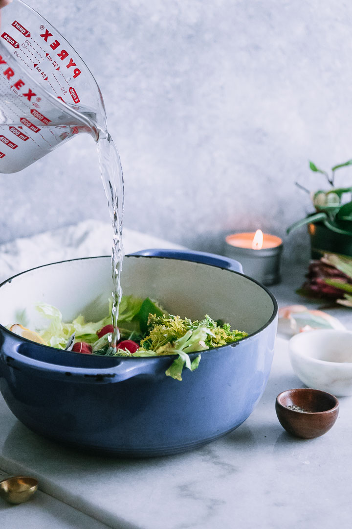 water pouring into a soup pot with vegetables and a candle in the background