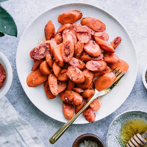a plate of roasted carrots on a blue table with a side of sea salt and a white napkin