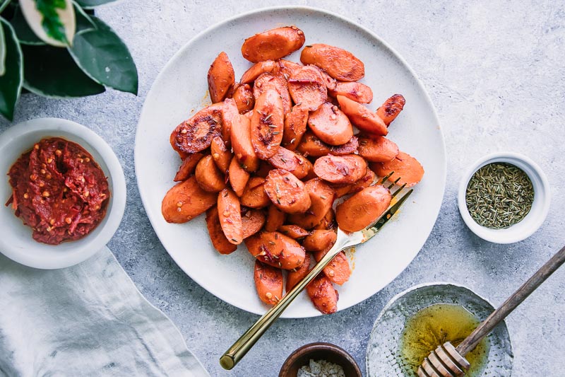 a plate of roasted carrots on a blue table with a side of sea salt and a white napkin